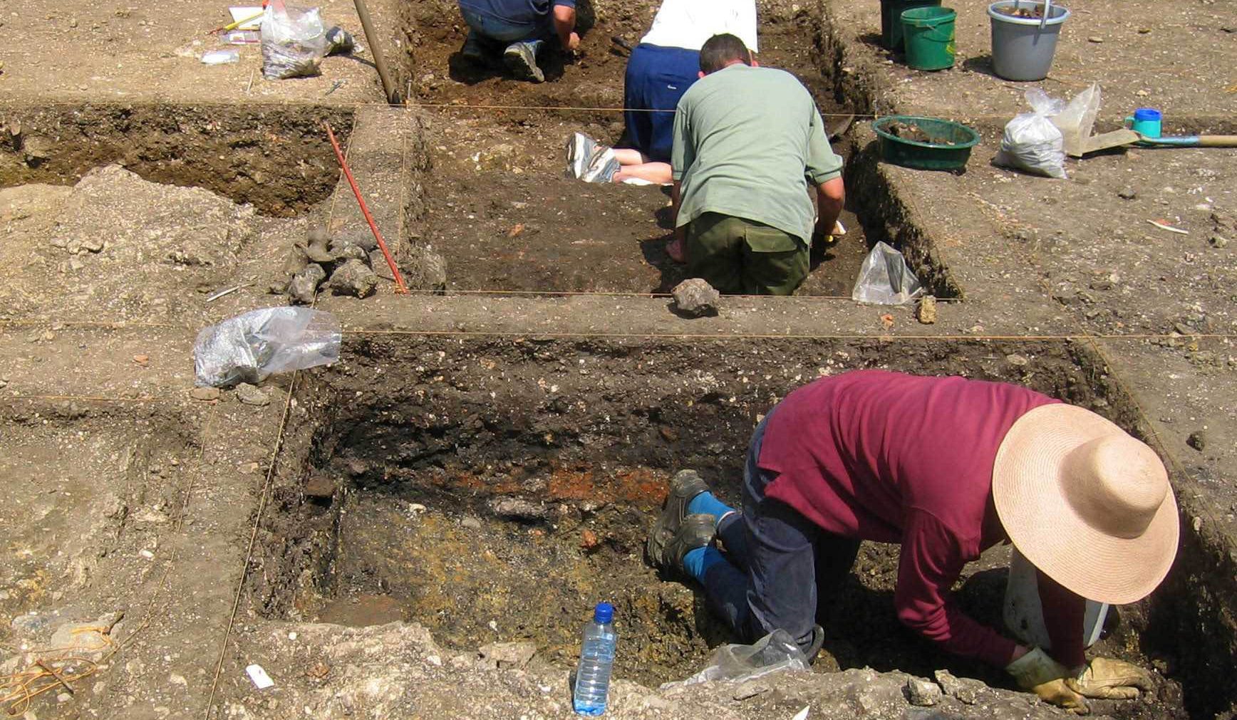 Four people digging in two trenches, surrounded by buckets, find bags, and water bottles.