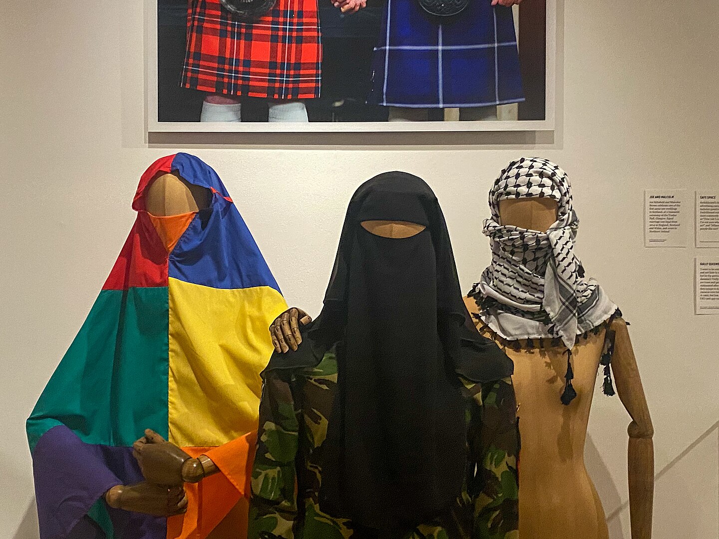 A rainbow khijmar is displayed alongside a camouflage shalwar kameez and a Palestinian Keffiyeh.